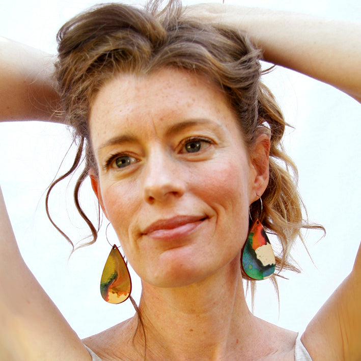 Model wearing wooden earrings shaped as a rain drop. Made from sustainable wood with stainless steel hoops. Made in Australia.